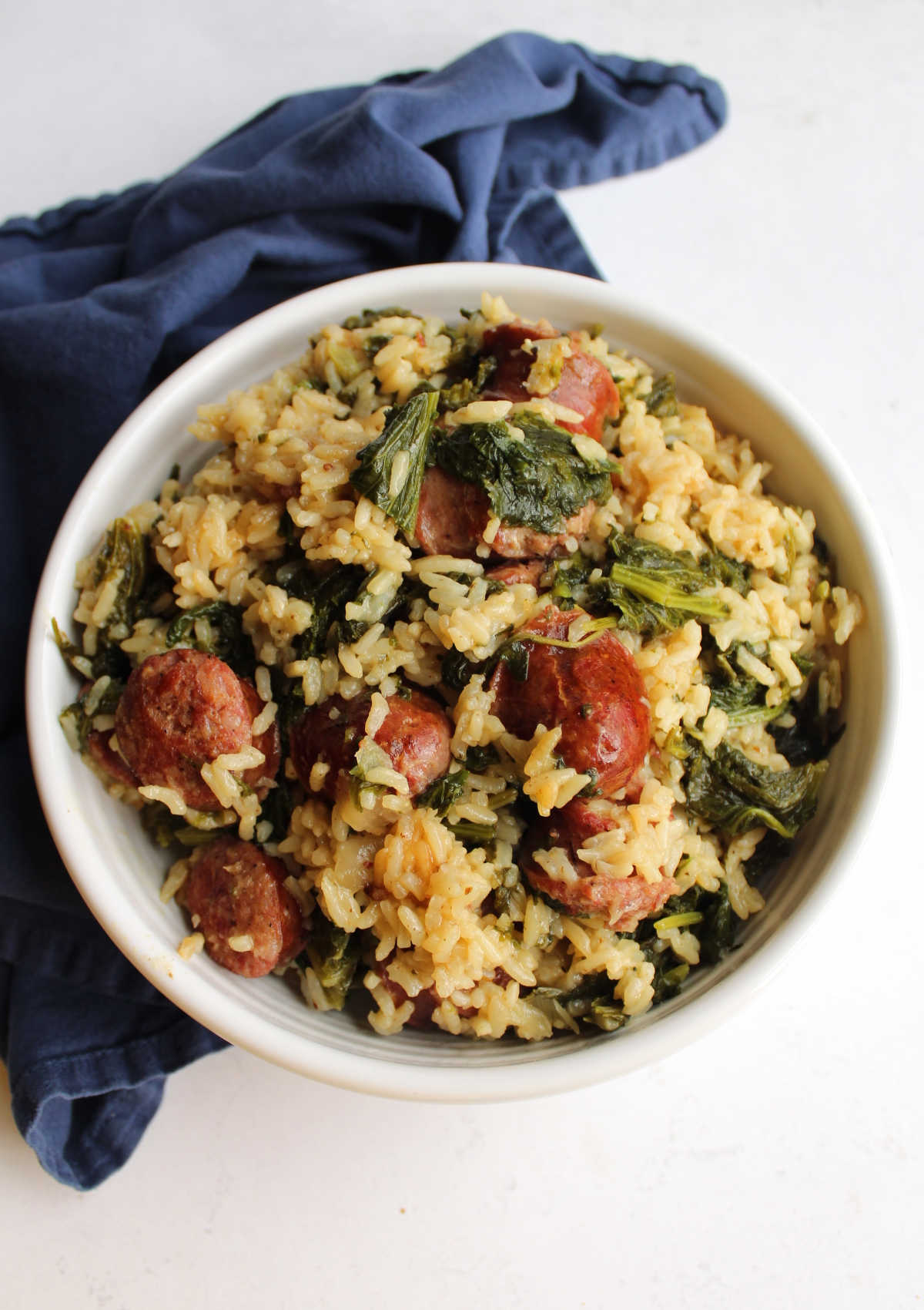 White serving bowl filled with rice, polish sausage and wilted mustard greens.