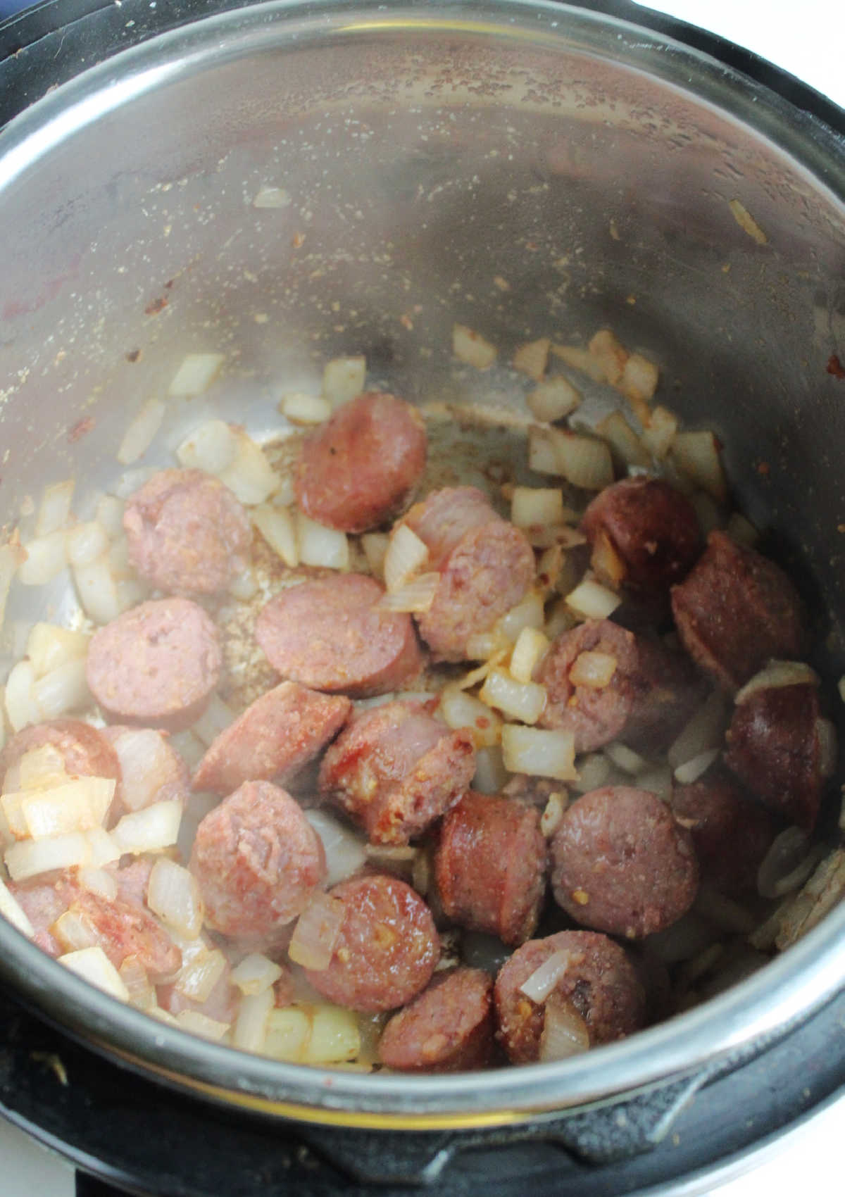 Looking inside instant pot showing browned pieces of kielbasa and softened onions.
