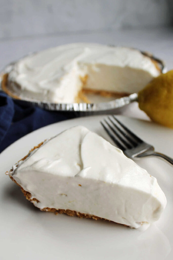 Slice of creamy no bake lemon pie on plate with remaining pie in background.