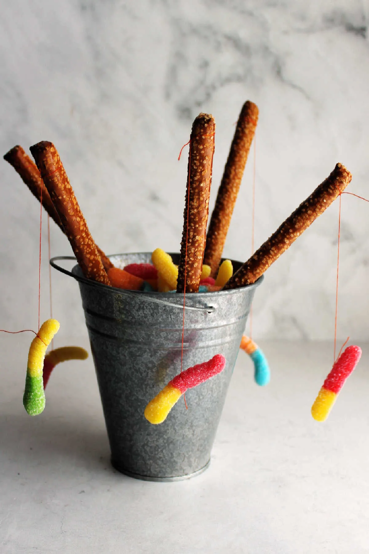 Small metal bucket with pretzel rods that look like fishing poles with gummy worms dangling from them.
