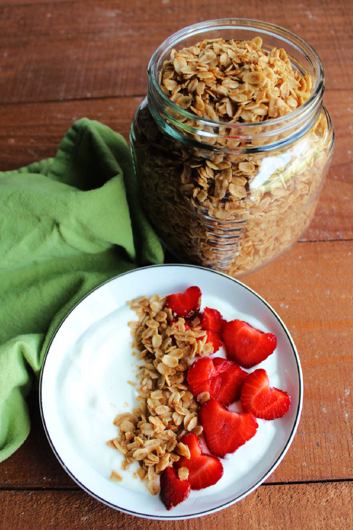 Jar of crock pot maple cinnamon granola next to bowl of yogurt topped with berries and granola.
