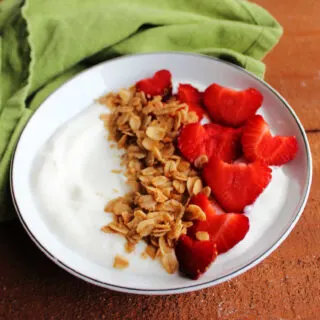 Bowl of yogurt topped with slow cooked maple granola and sliced strawberries.