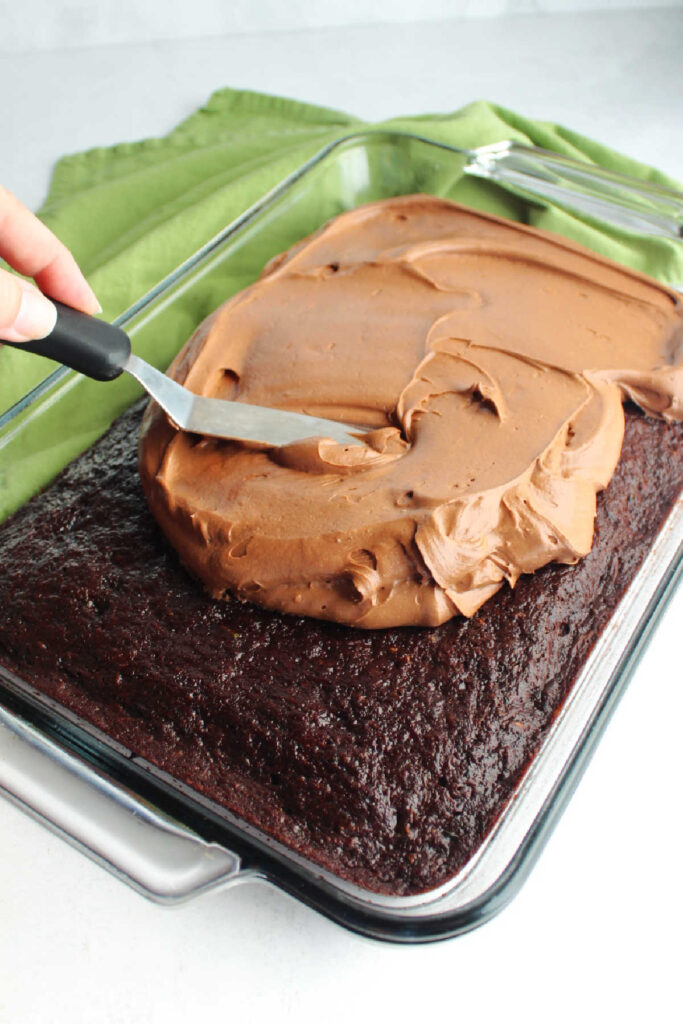 Spreading chocolate cream cheese frosting over baked chocolate zucchini cake.