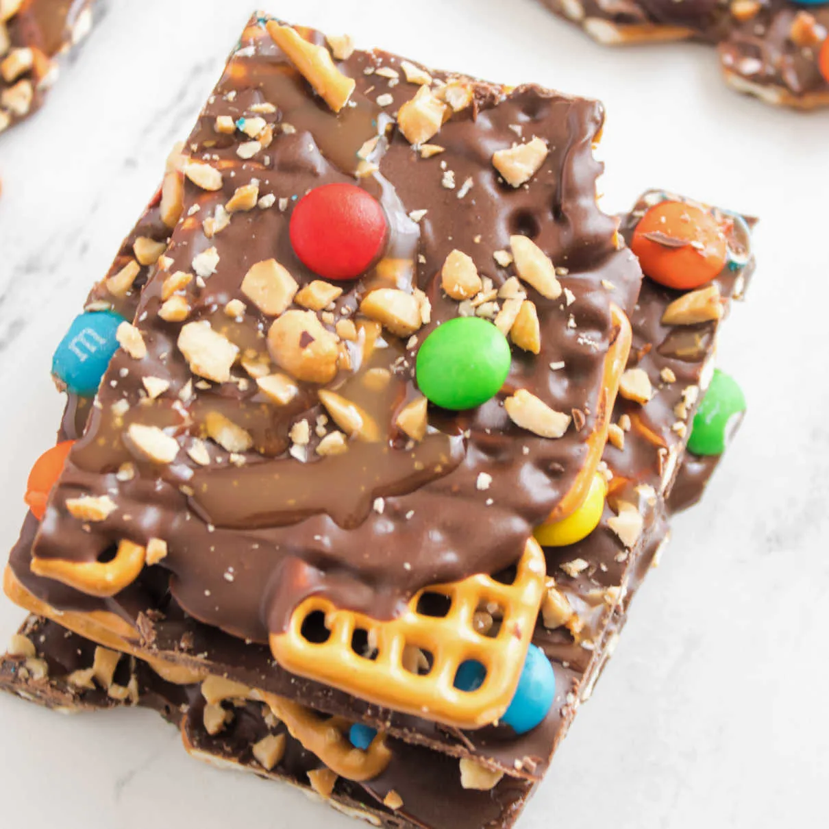 Close up of chocolate pretzel bark with caramel drizzle, chopped peanuts and m&ms on top.