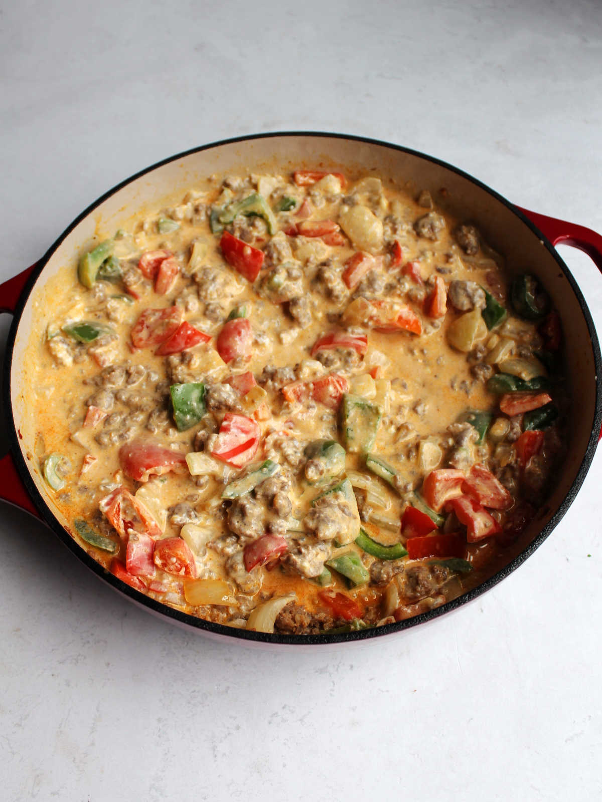 Creamy cheesy sauce with chorizo and vegetables in pan.