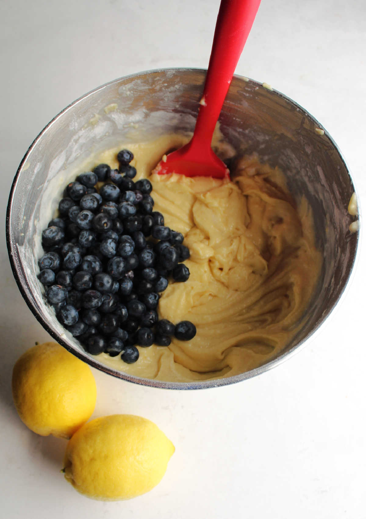 Mixing bowl of lemon cake batter with fresh blueberries ready to be stirred in.