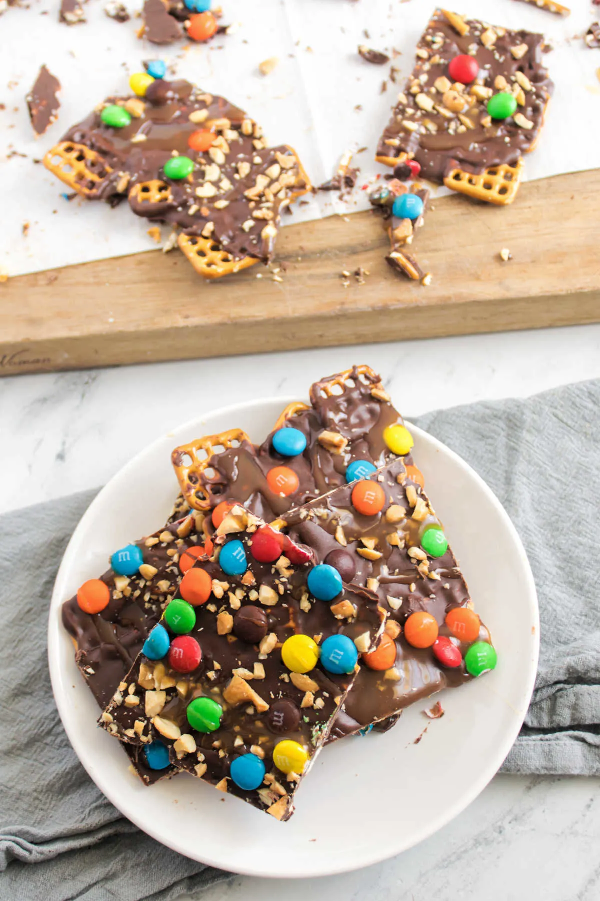 chocolate pretzel bark broken into pieces on cutting board with some on a plate.