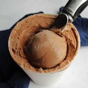 Ice cream scoop scooping a ball of homemade chocolate ice cream out of the storage container.