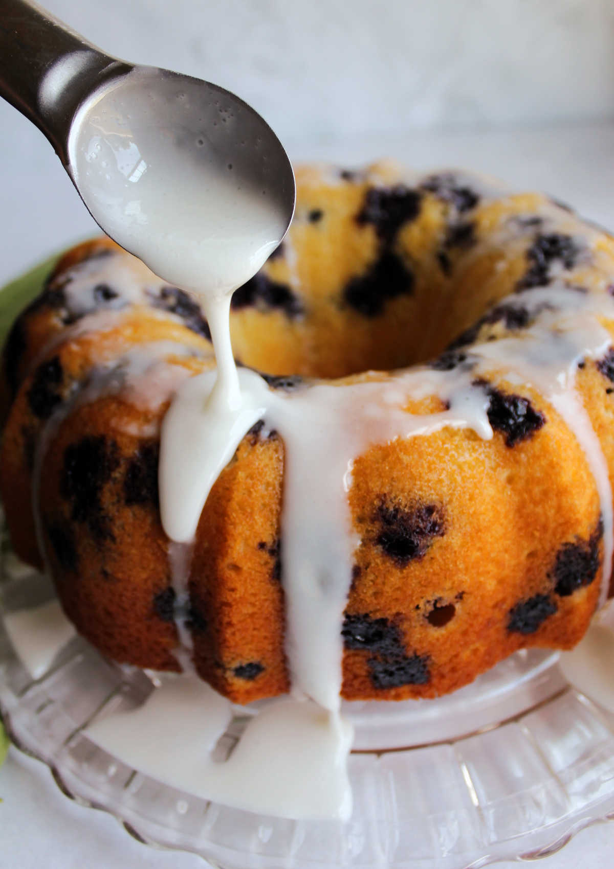 Spooning lemon and powdered sugar glaze over blueberry bundt cake.