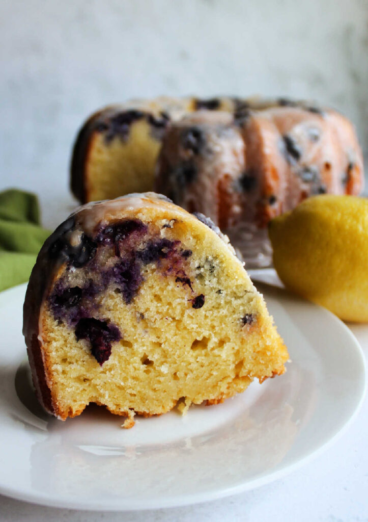 Slice of lemon blueberry bundt cake standing on dessert plate. with lots of blueberries showing.