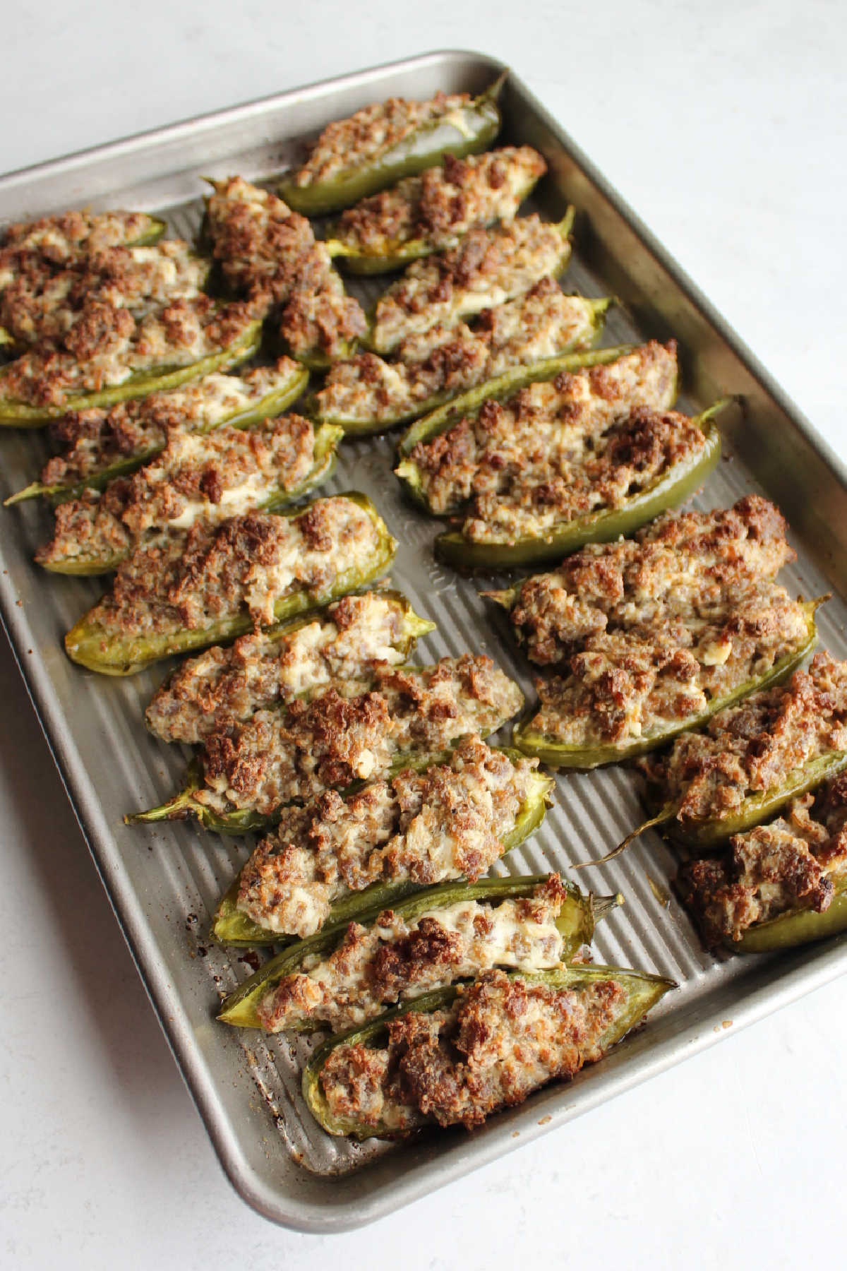 Tray of sausage stuffed jalapeno poppers with golden brown tops fresh from the oven.