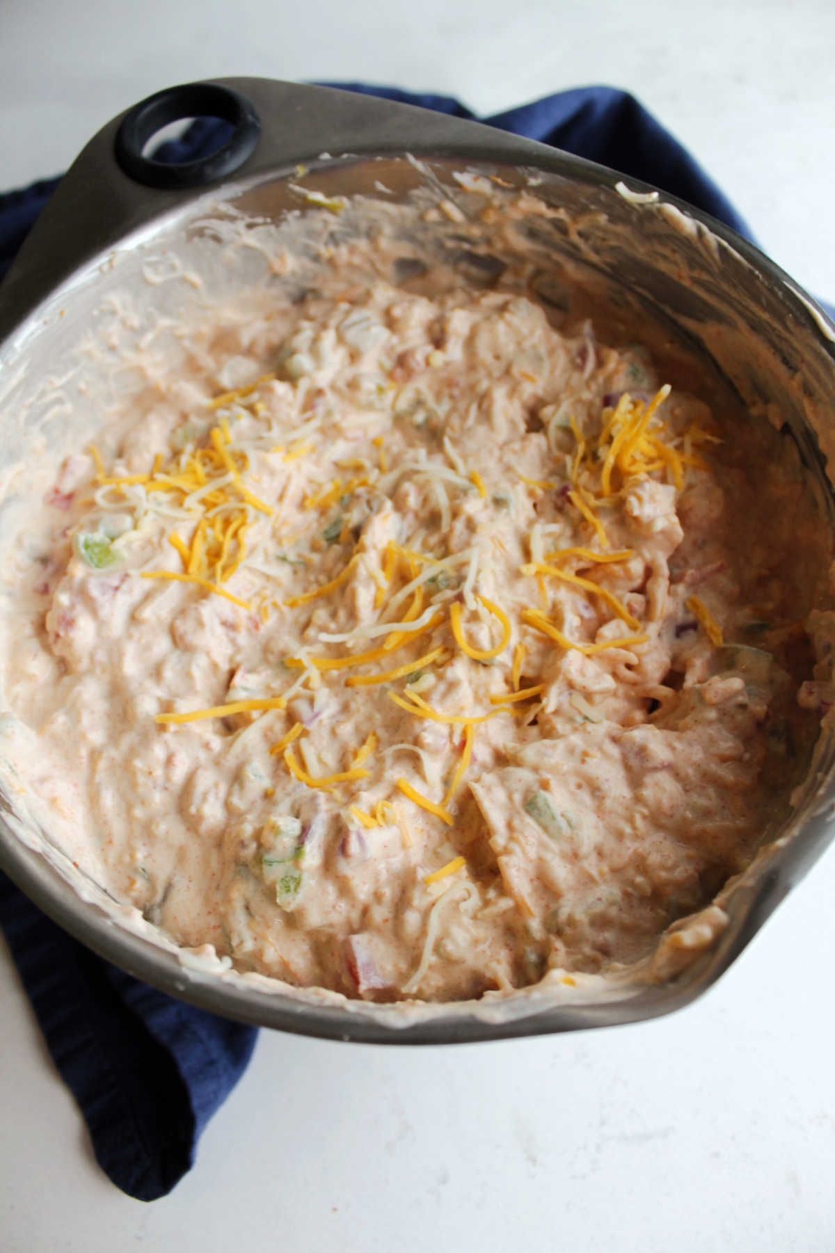 Adding shredded cheese to dip in large mixing bowl.