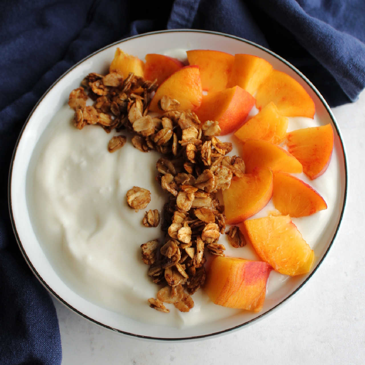 Bowl of yogurt topped with chunks of fresh peach and maple cinnamon granola.