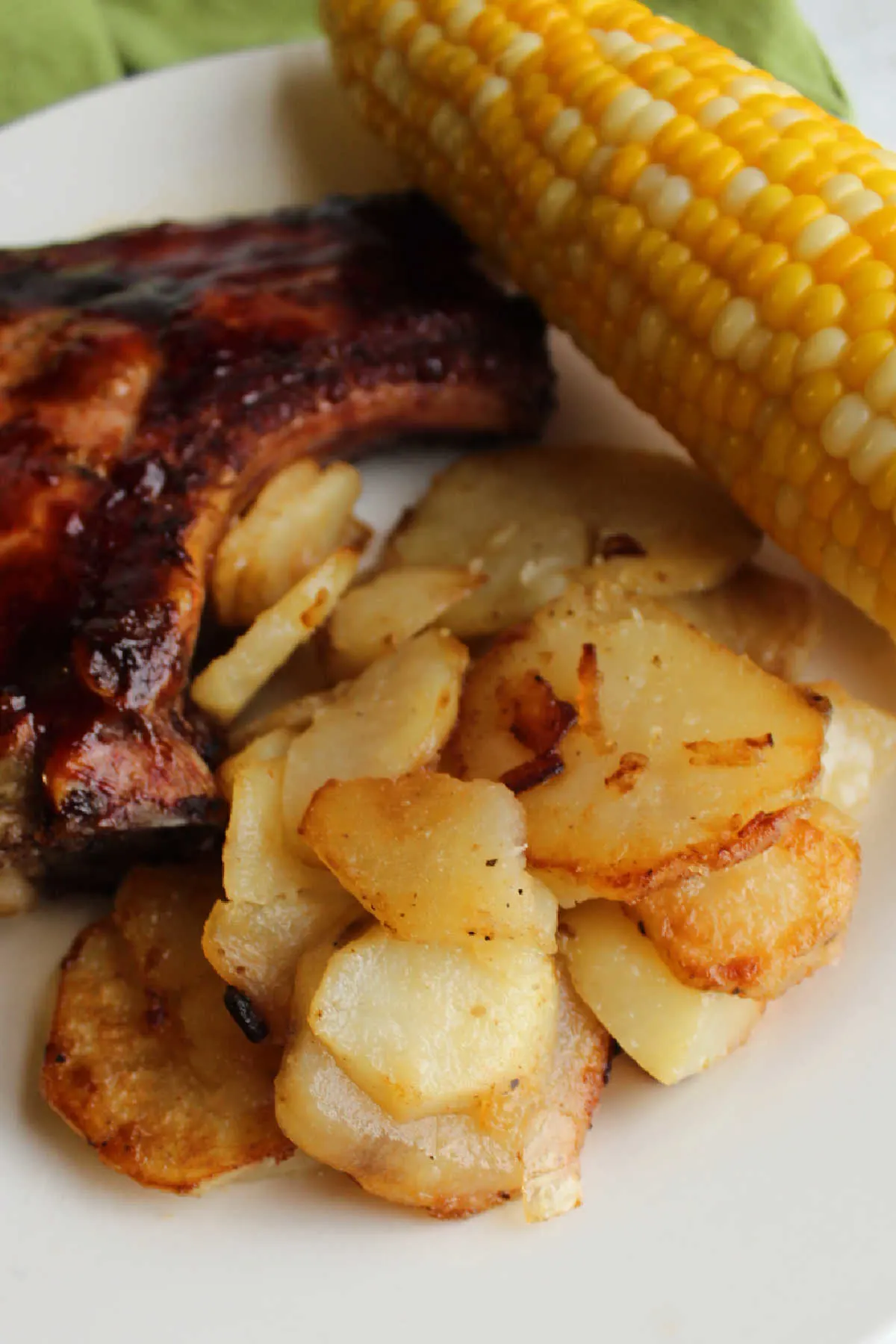 Close up of fried potatoes on plate with corn and pork chop in background.