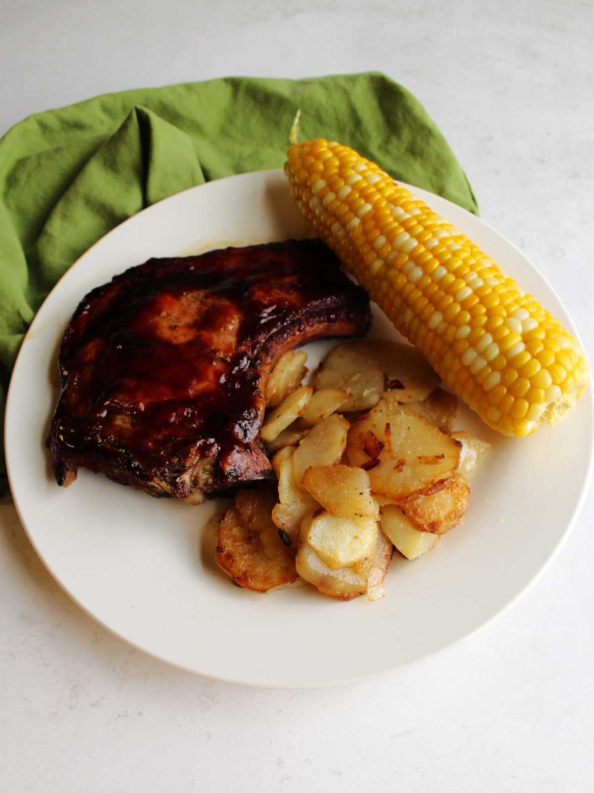 Plate of fried potatoes, BBQ pork chop and corn on the cob.