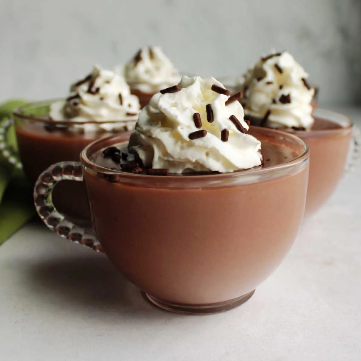 Glass mugs filled with hot chocolate pudding topped with whipped cream and chocolate sprinkles.
