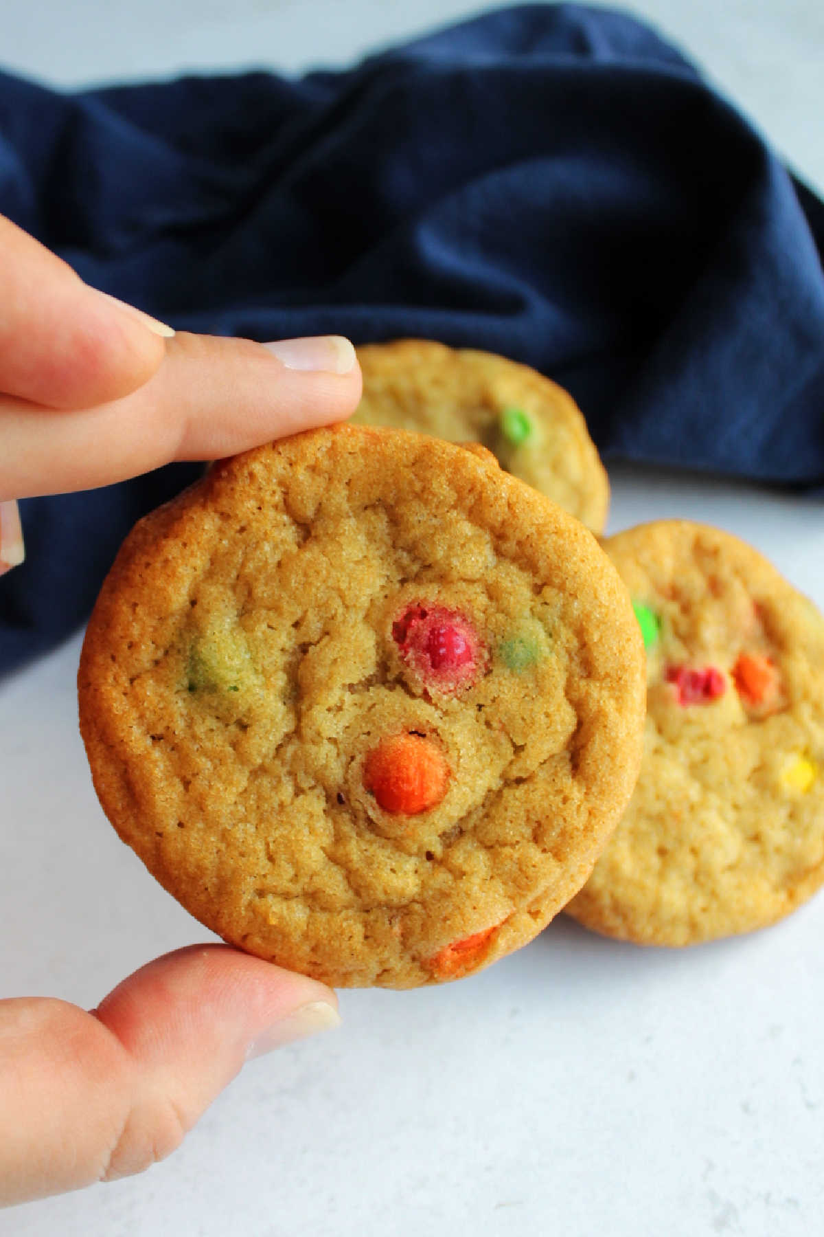 Hand holding M&M cookie, ready to eat.