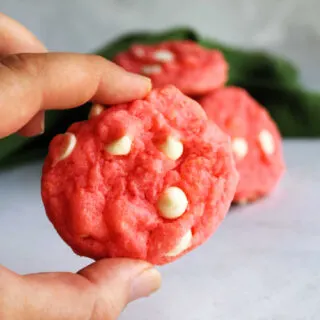Hand holding a pink strawberry cake mix cookie with white chocolate chips.