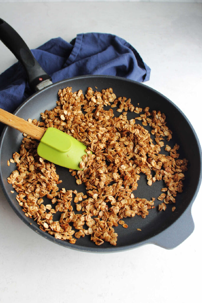 Large skillet filled with freshly make maple cinnamon granola and spatula.