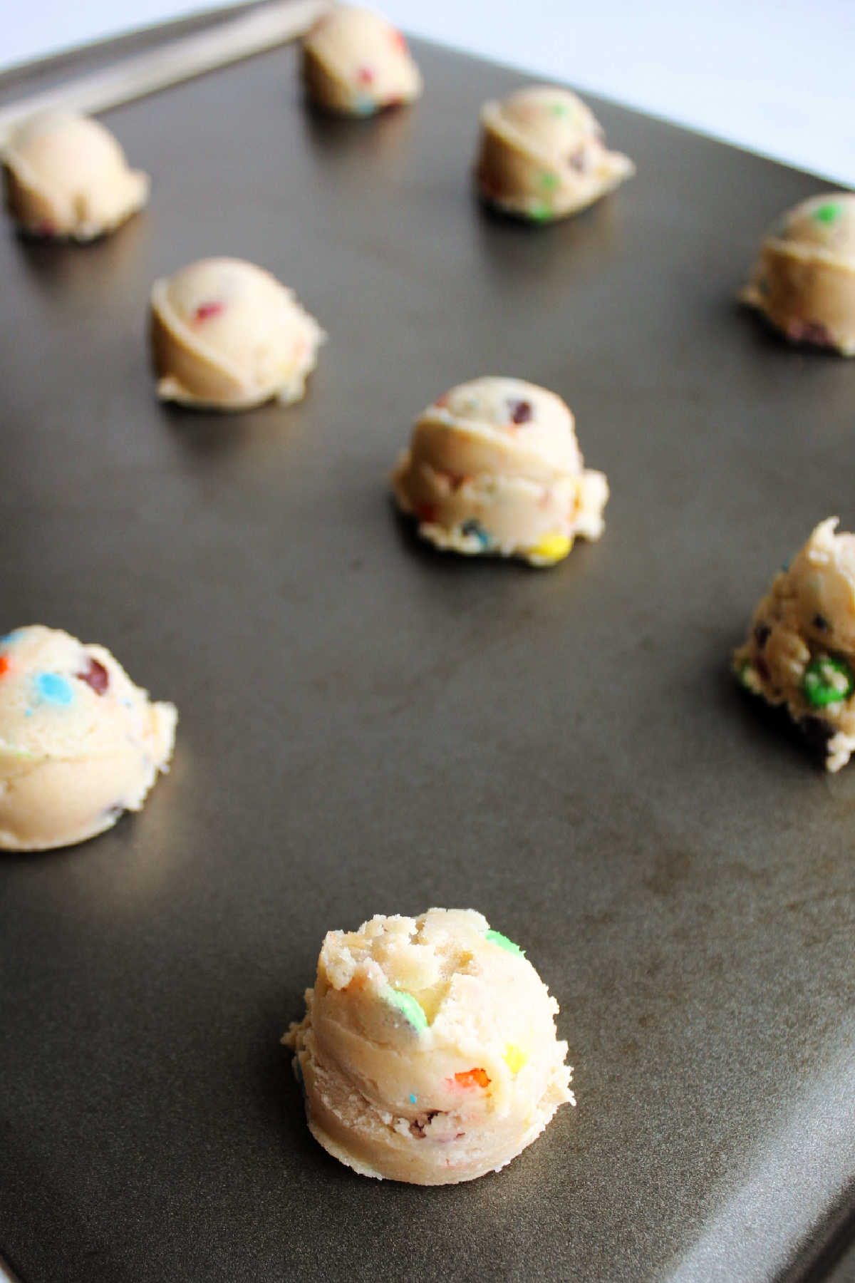 Scoops of m&m cookie dough on baking sheet.