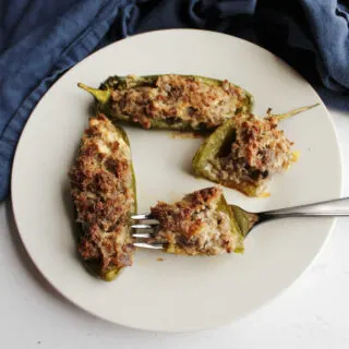 Plate of jalapeno pepper halves stuffed with sausage and cream cheese with a bite on a fork ready to eat.