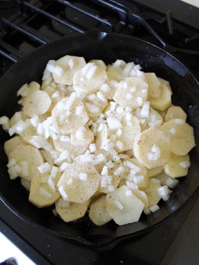 Cast iron skillet with sliced potatoes and diced onions.