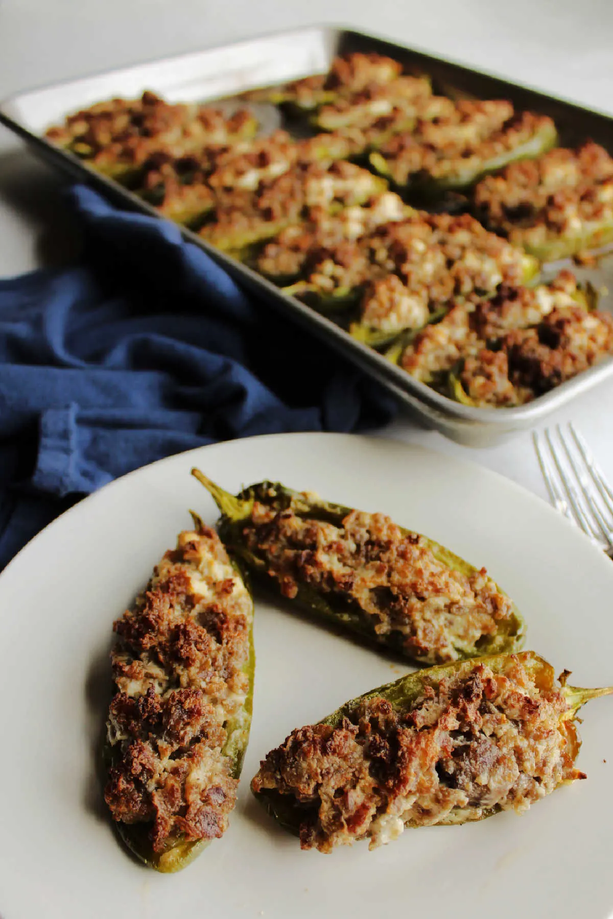 plate of creamy sausage stuffed jalapeno peppers in front of tray of remaining poppers.