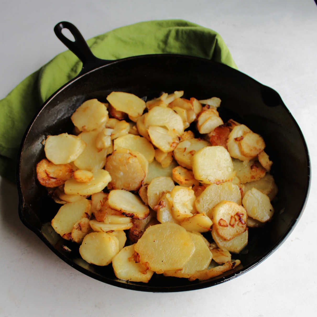 Large cast iron skillet filled with fried sliced potatoes.