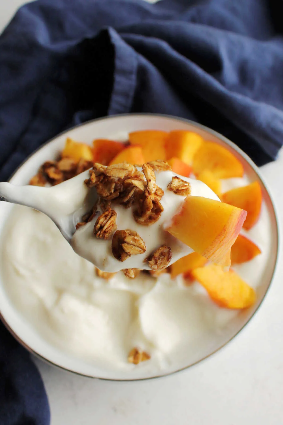 Spoonful of yogurt with skillet granola and a chunk of fresh peach, ready to eat.