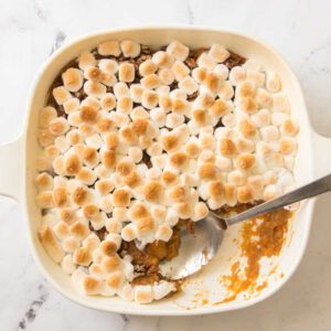 Square casserole dish filled with a layer of mashed sweet potatoes topped with pecans and gold brown marshmallows.