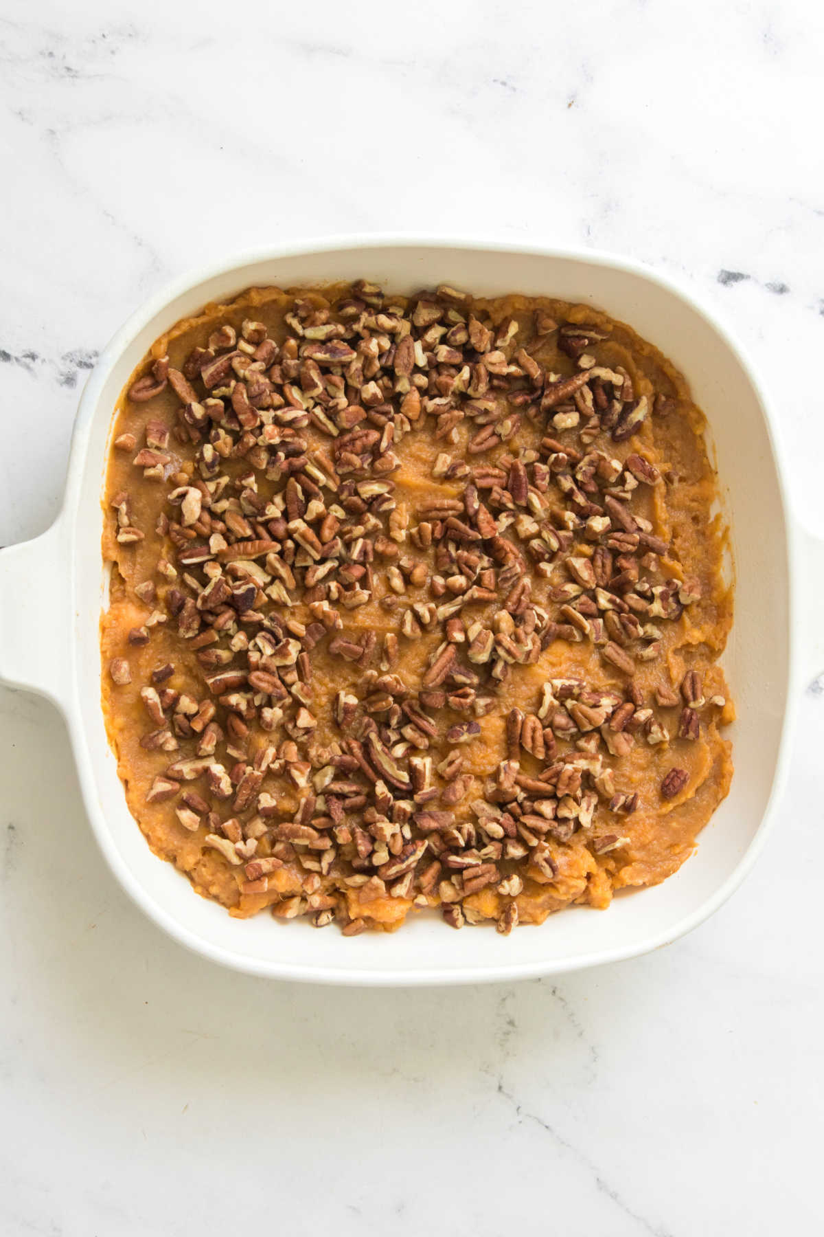 Casserole dish filled with mashed sweet potatoes and sprinkled with pecans.