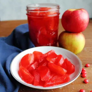 Close up of small bowl of bright red stewed apple slices next to a jar of candied apples.