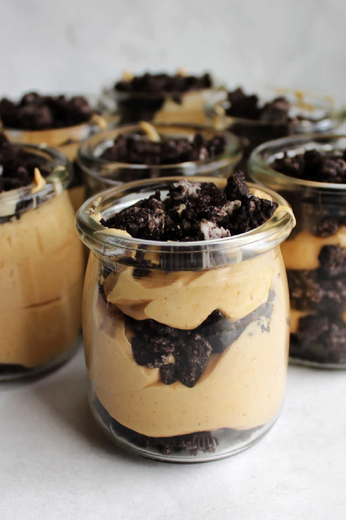 Small glass yogurt jars filled with layered chocolate cookie crumbs and peanut butter filling.