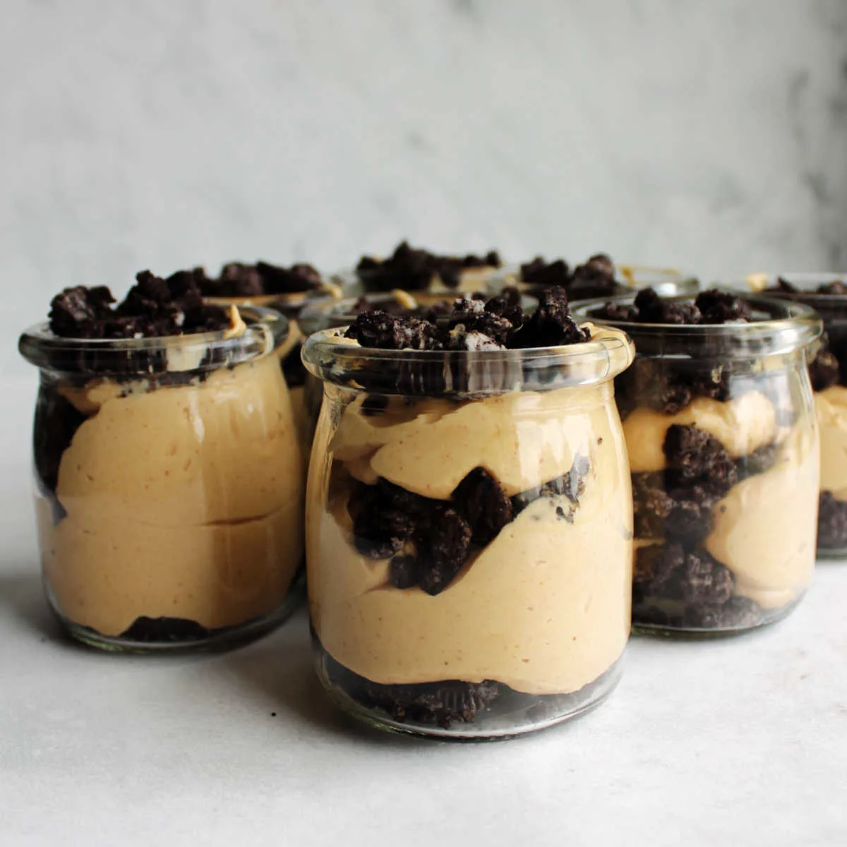 Small glass jars filled with layers of Oreo crumbs and fluffy peanut butter filling.