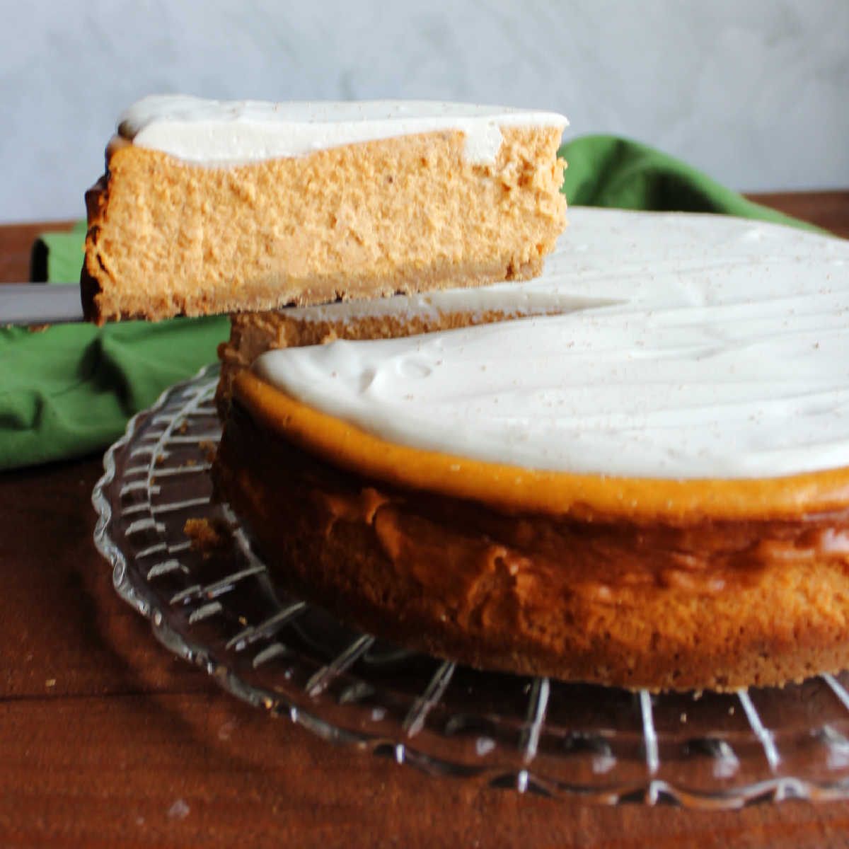 Lifting slice of pumpkin cheesecake topped with white sour cream topping out of the whole cake.