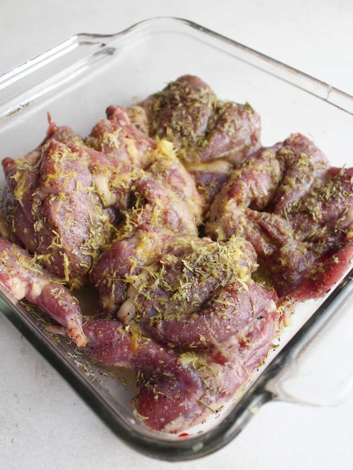 Baking dish filled with raw quail coated in lemon and rosemary marinade mixture.