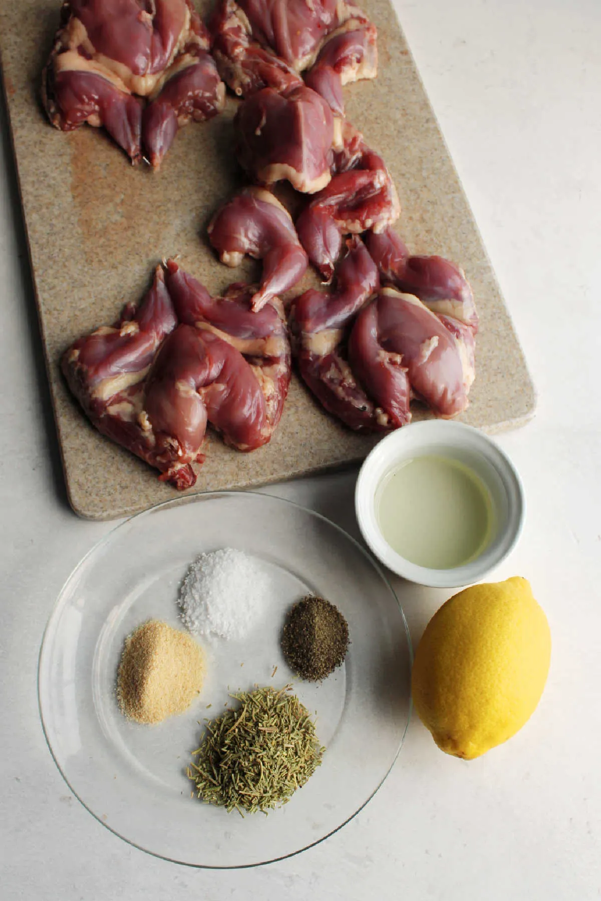 Ingredients for roasted quail including quail, lemon, oil, rosemary, garlic powder, salt and pepper.