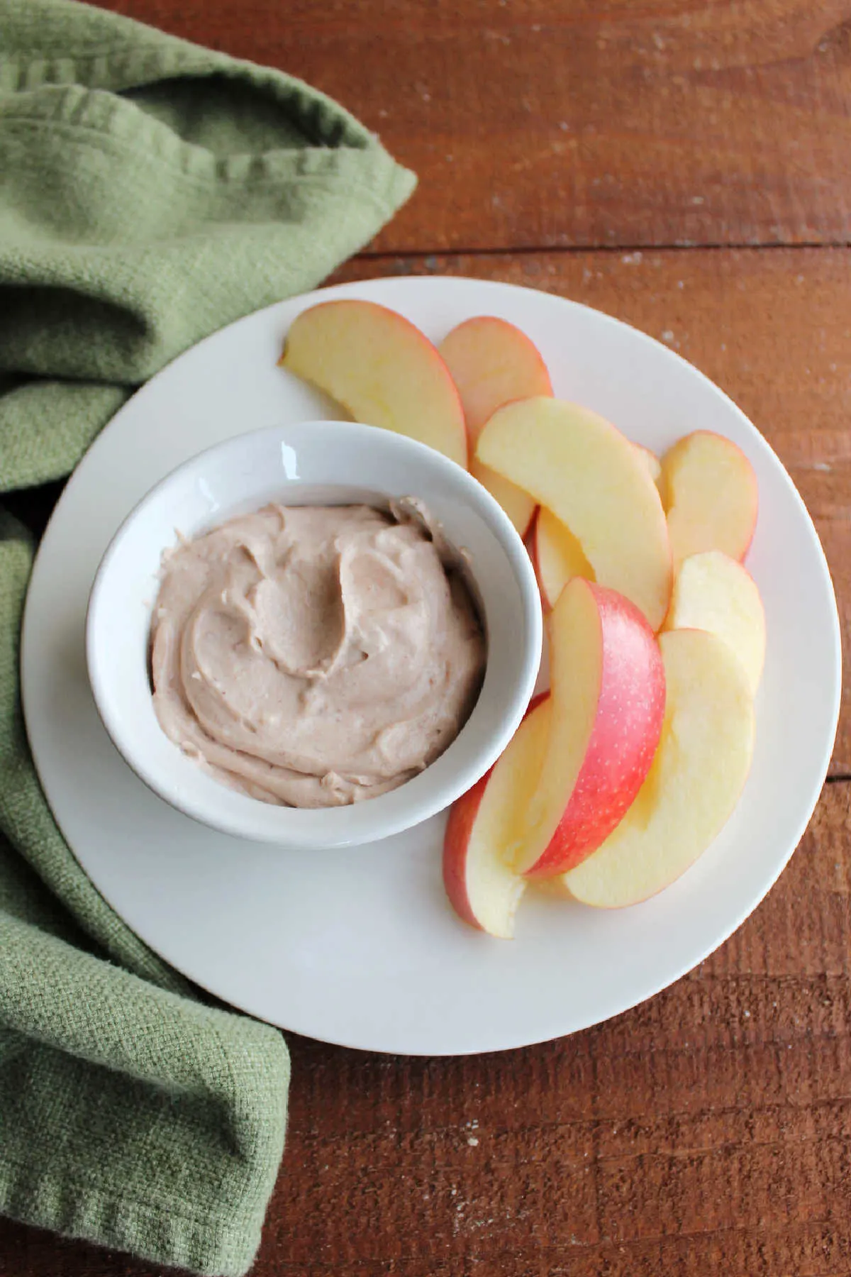 Ramekin of creamy apple butter fruit dip served on plate with apple slices.