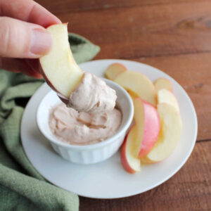 Hand holding apple slice with generous amount of smooth and creamy apple butter dip on the end.