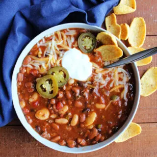 Bowl of venison chili with lots of beans topped with shredded cheese, jalapenos and a dollop of sour cream.