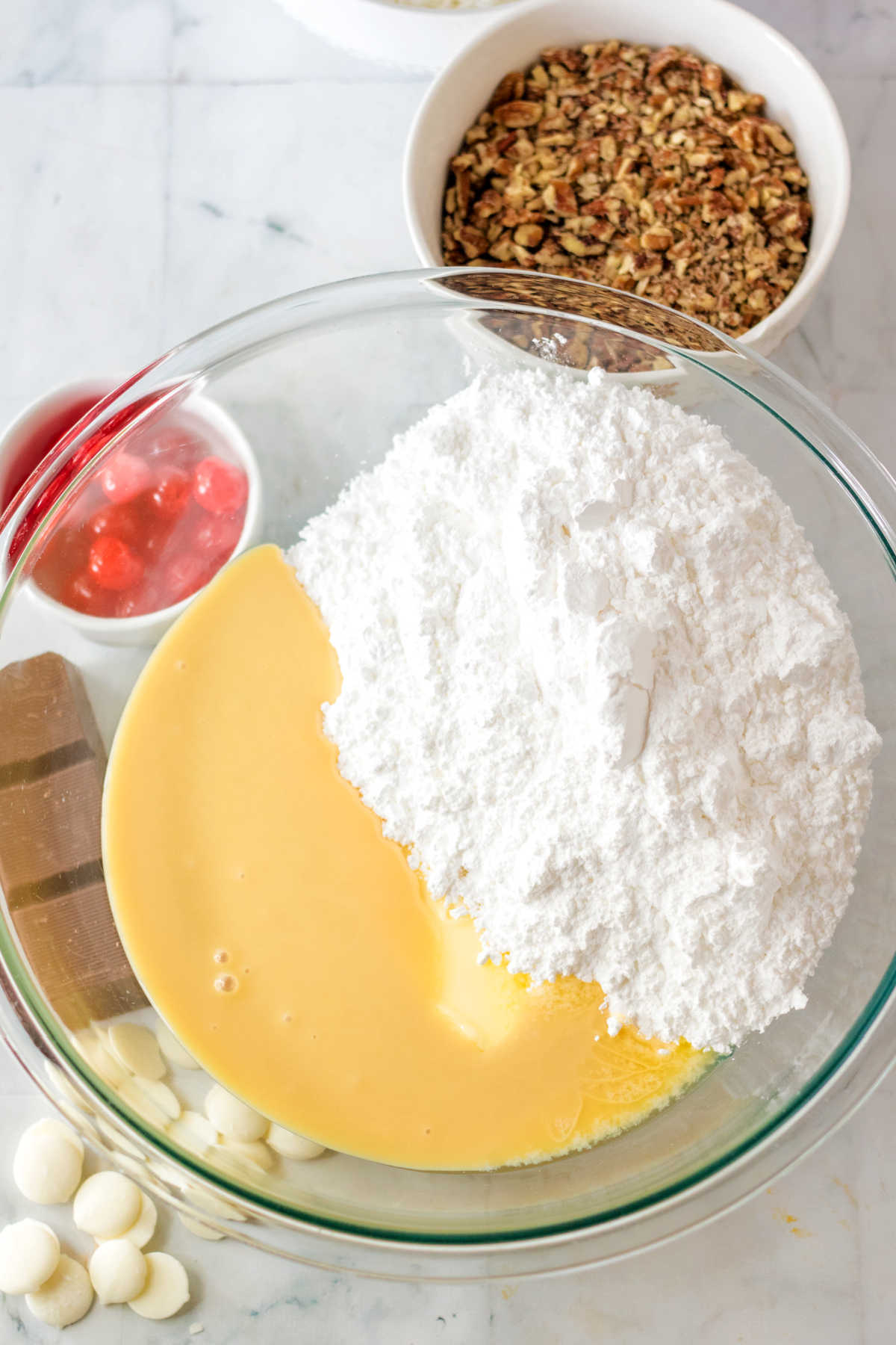 Glass mixing bowl filled with powdered sugar, condensed milk and butter.