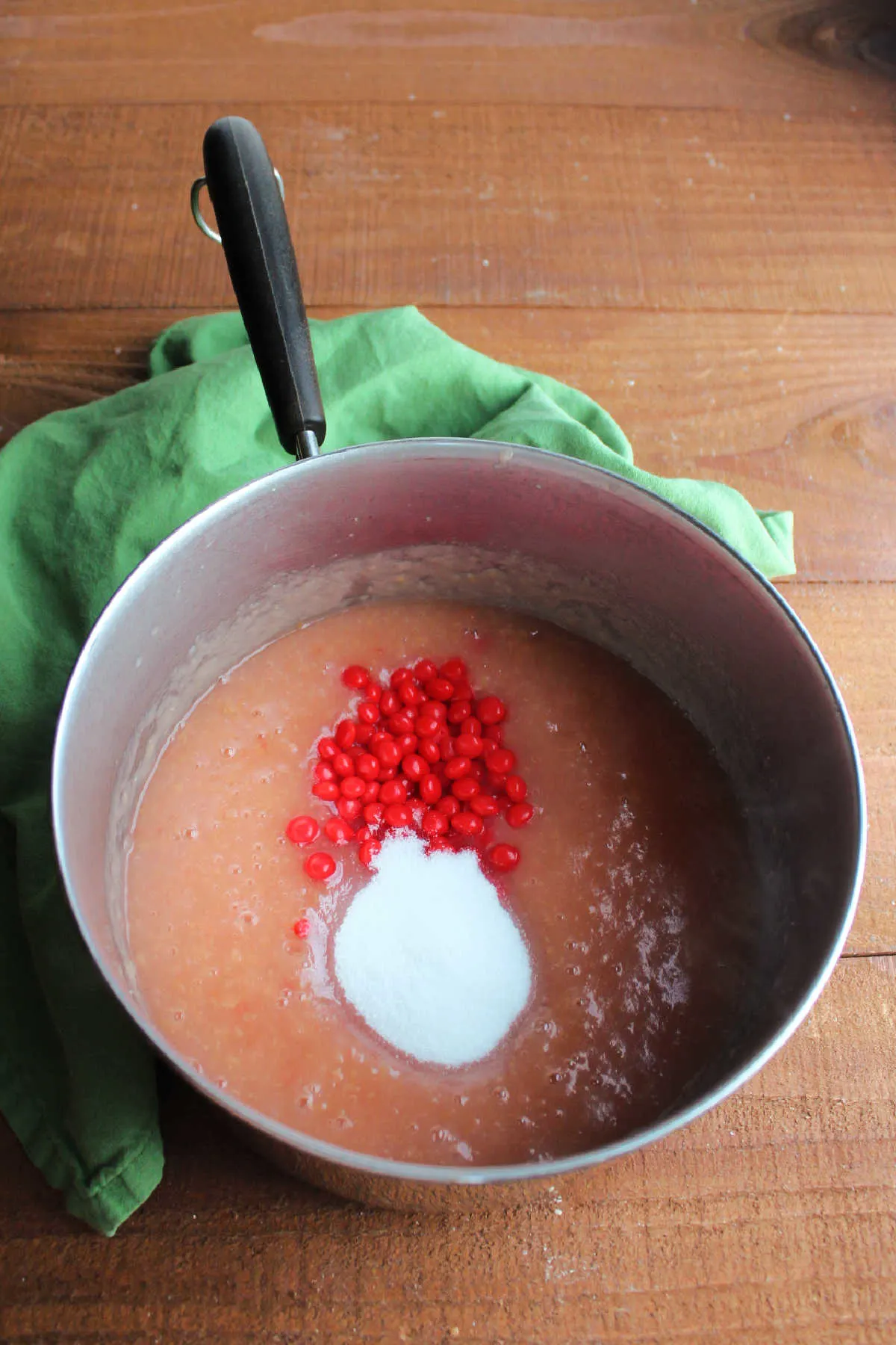 Adding sugar and Red Hot candies to saucepan of pink applesauce.