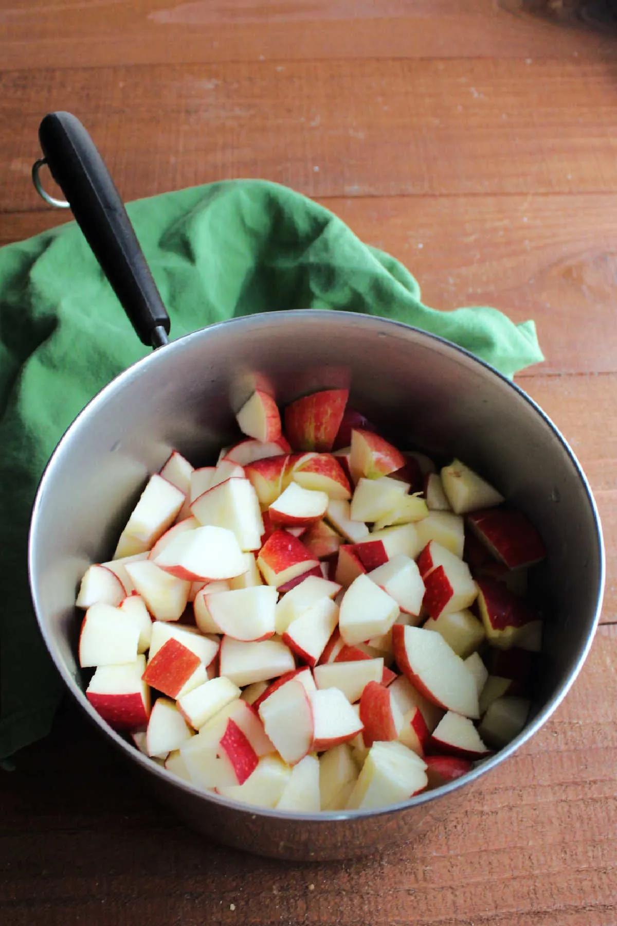 Chunks of apple with peel on them in saucepan with water ready to cook.