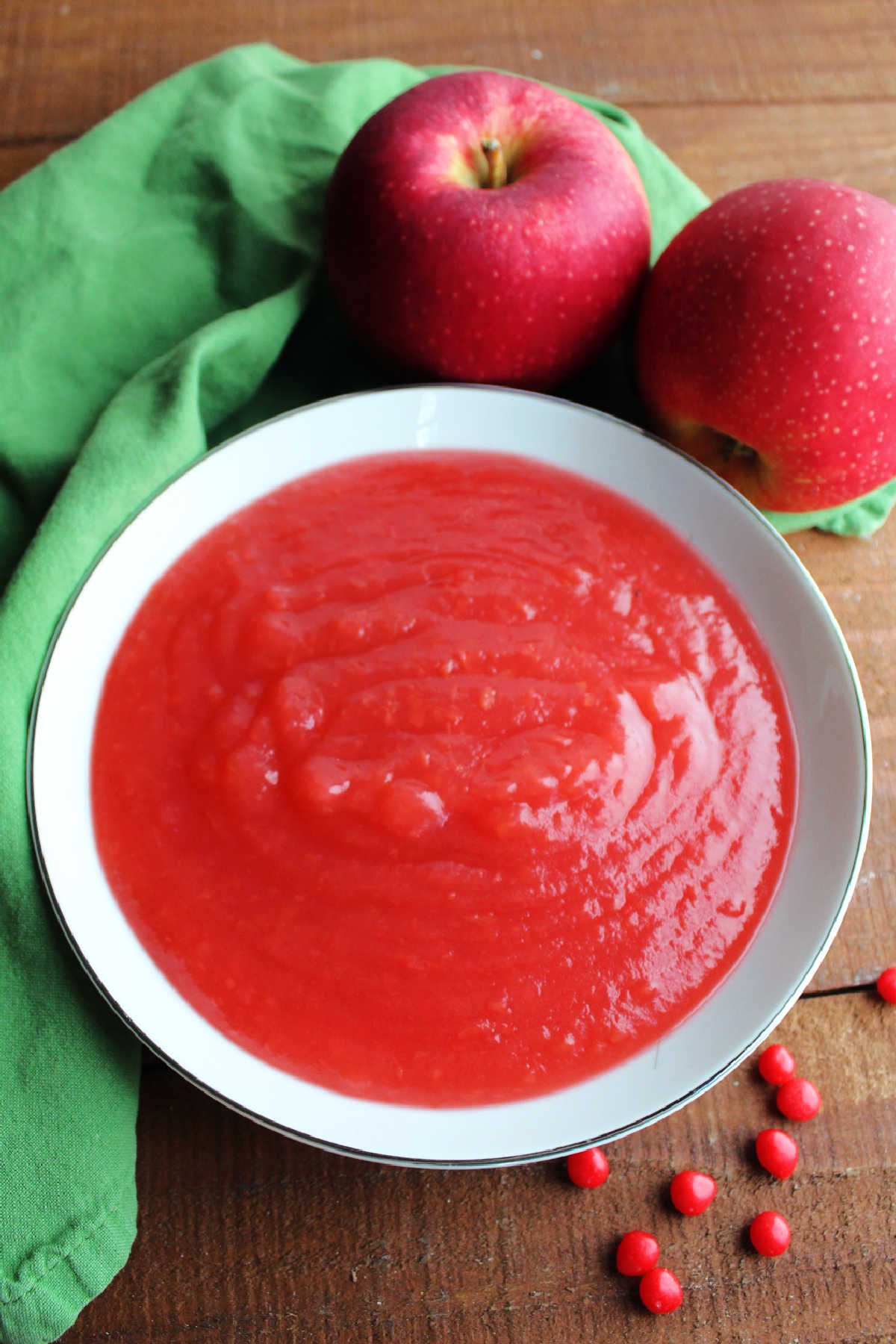 Bowl of homemade red hot applesauce with fresh apples and red hot candies nearby.