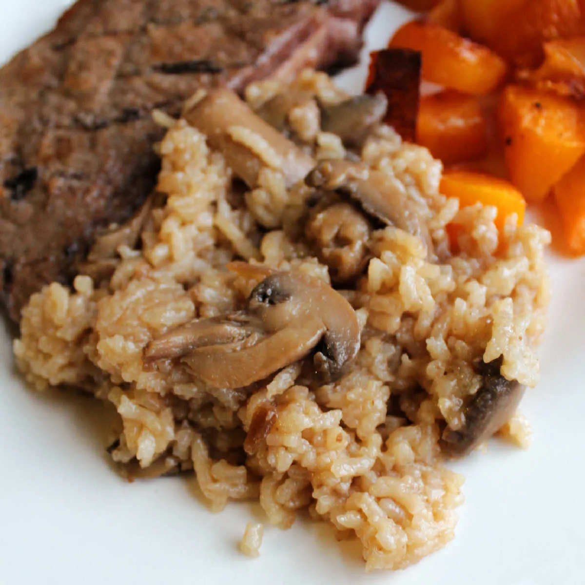 Close up of fluffy baked rice with beef broth and mushrooms served on dinner plate.