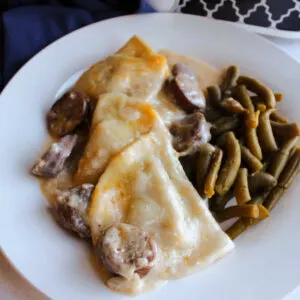 Close up of cheesy pirogies and chunks of kielbasa in a sour cream sauce served with green beans.