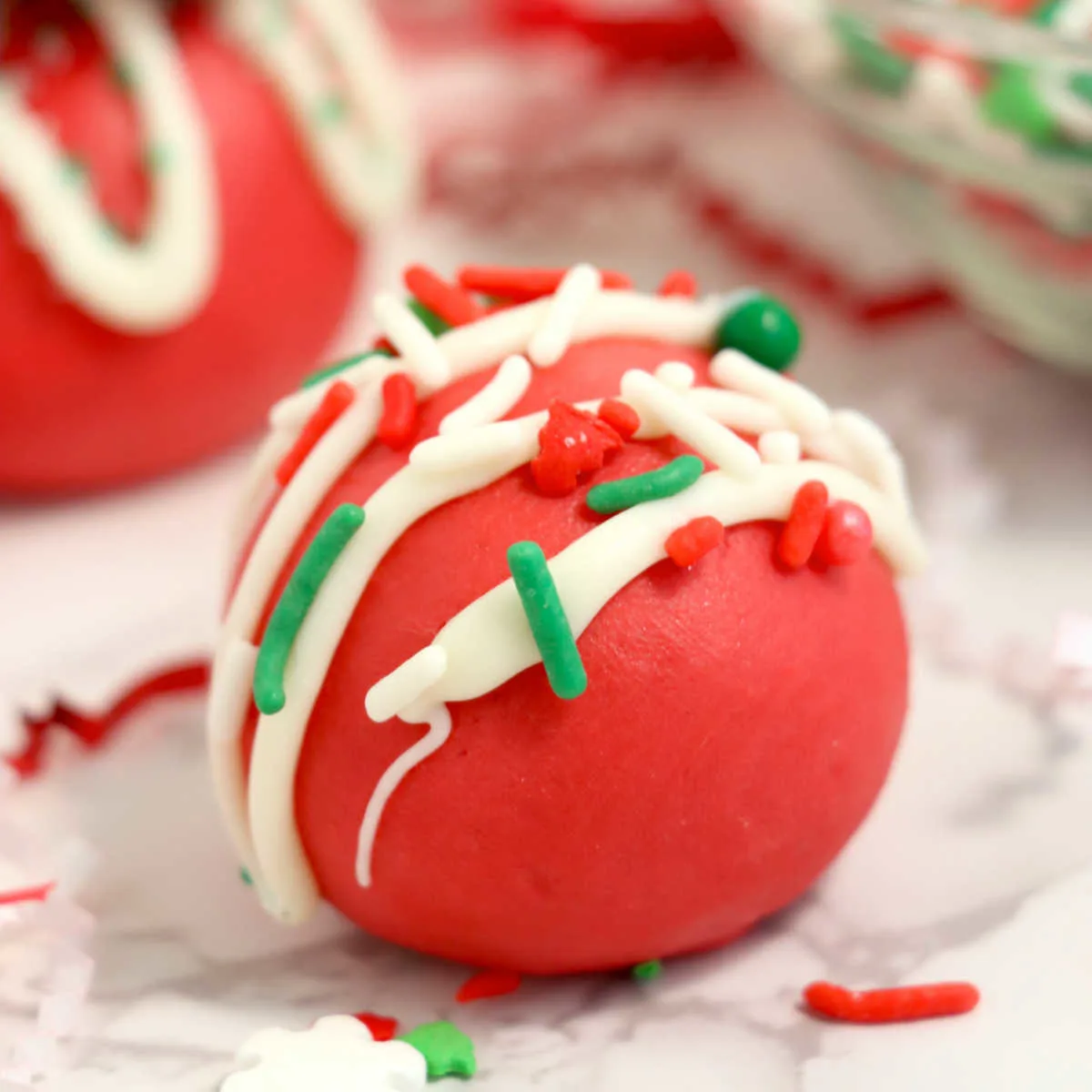 Close up of smooth red velvet truffles topped with white chocolate drizzle and Christmas sprinkles.