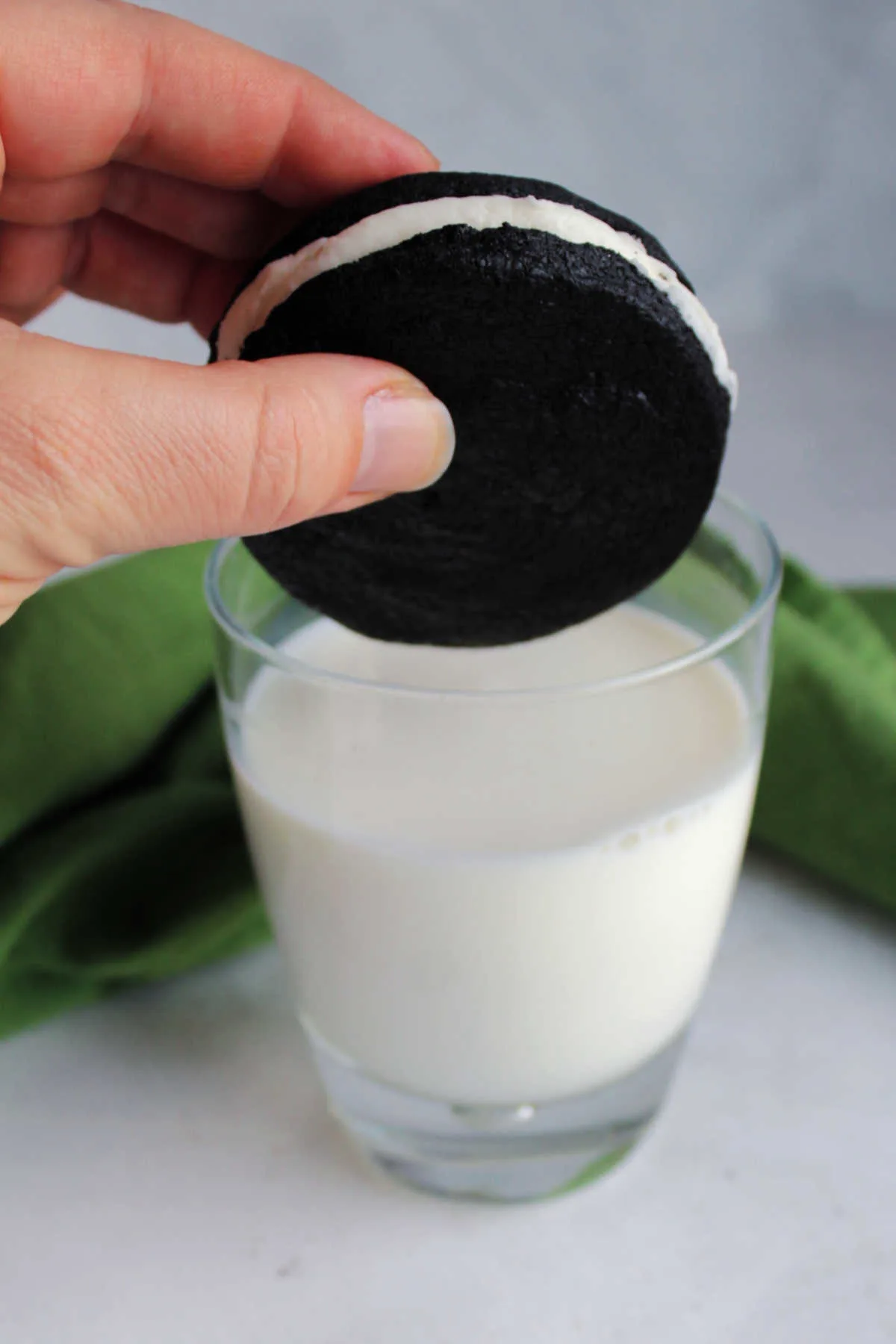 Hand getting ready to dunk a dark chocolate sandwich cookie with white cream filling into a glass of milk.