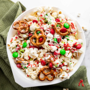 Bowl of Christmas popcorn mix with pretzels, M&Ms, white chocolate and sprinkles.