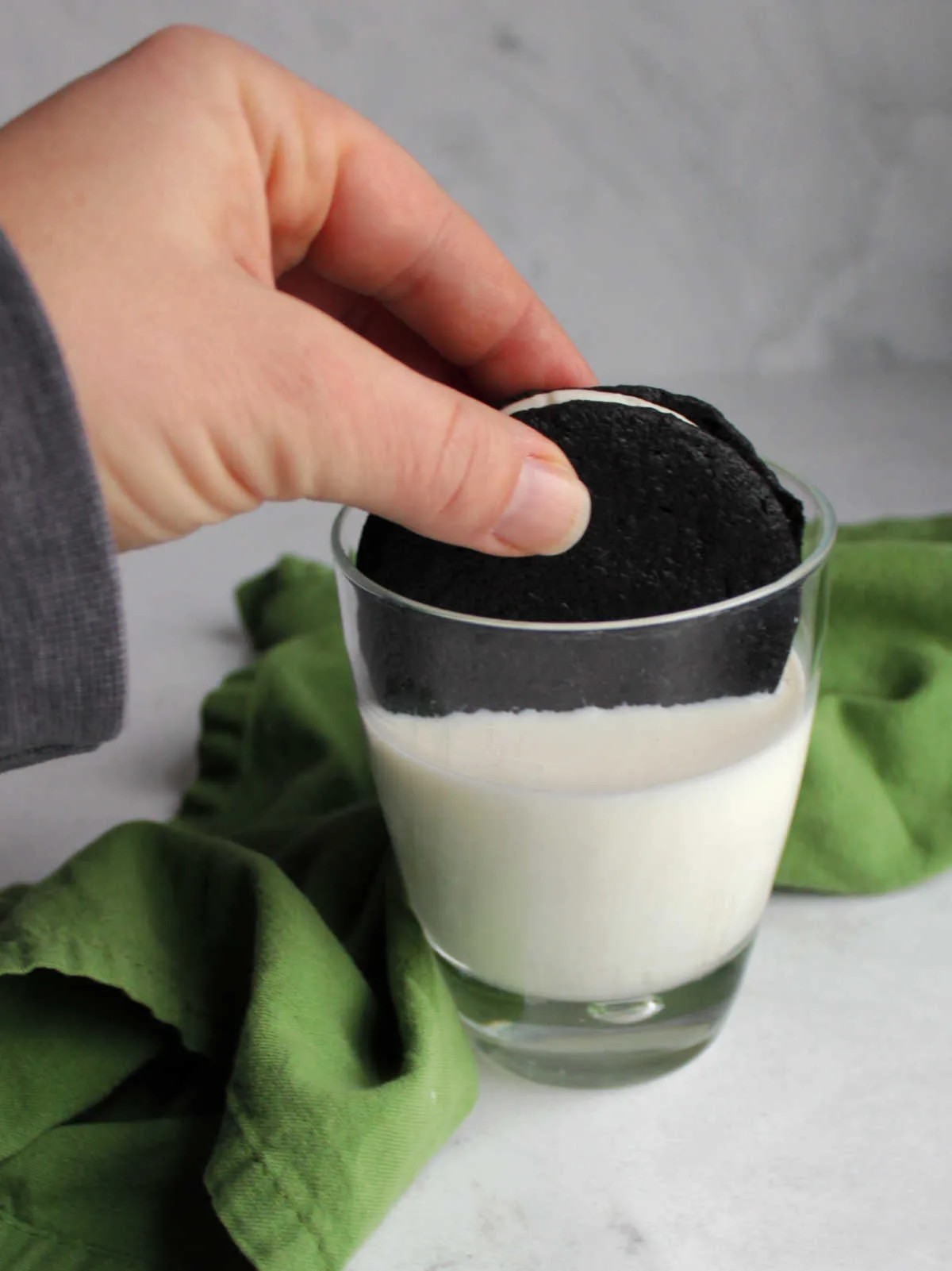 Hand holding homemade oreo cookie submerged in glass of milk. 